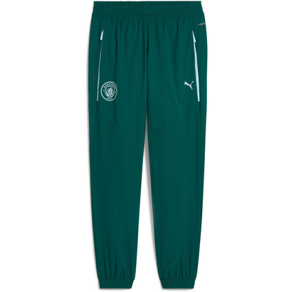 PUMA MANCHESTER CITY PUMATECH WOVEN PANTS 2025 2026 groen trainingsbroek met lichtblauw detail en clublogo van Manchester City op licht blauw achtergrond Kickoff Antwerpen voetbalshop football store