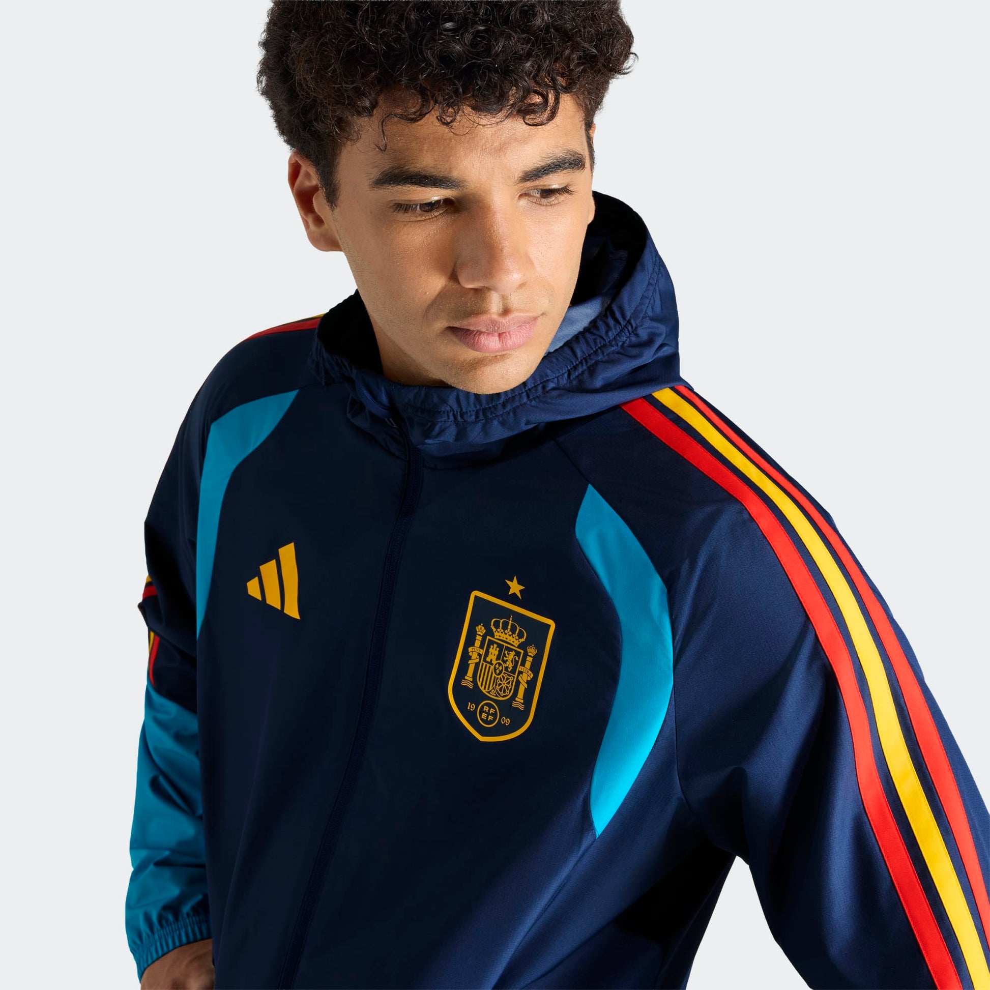 Adidas RFEF Spanje All-Weather Regenjas blauw met RFEF-logo en rode geel strepen WK 2026 collectie Kickoff Antwerpen voetbalshop