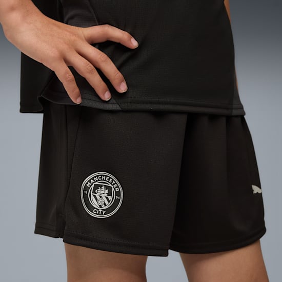 Puma Manchester City training short jeugd 2025 2026 met zakken en DryCELL logo, exclusief verkrijgbaar bij Kickoff Antwerpen, de voetbalshop van Antwerpen.